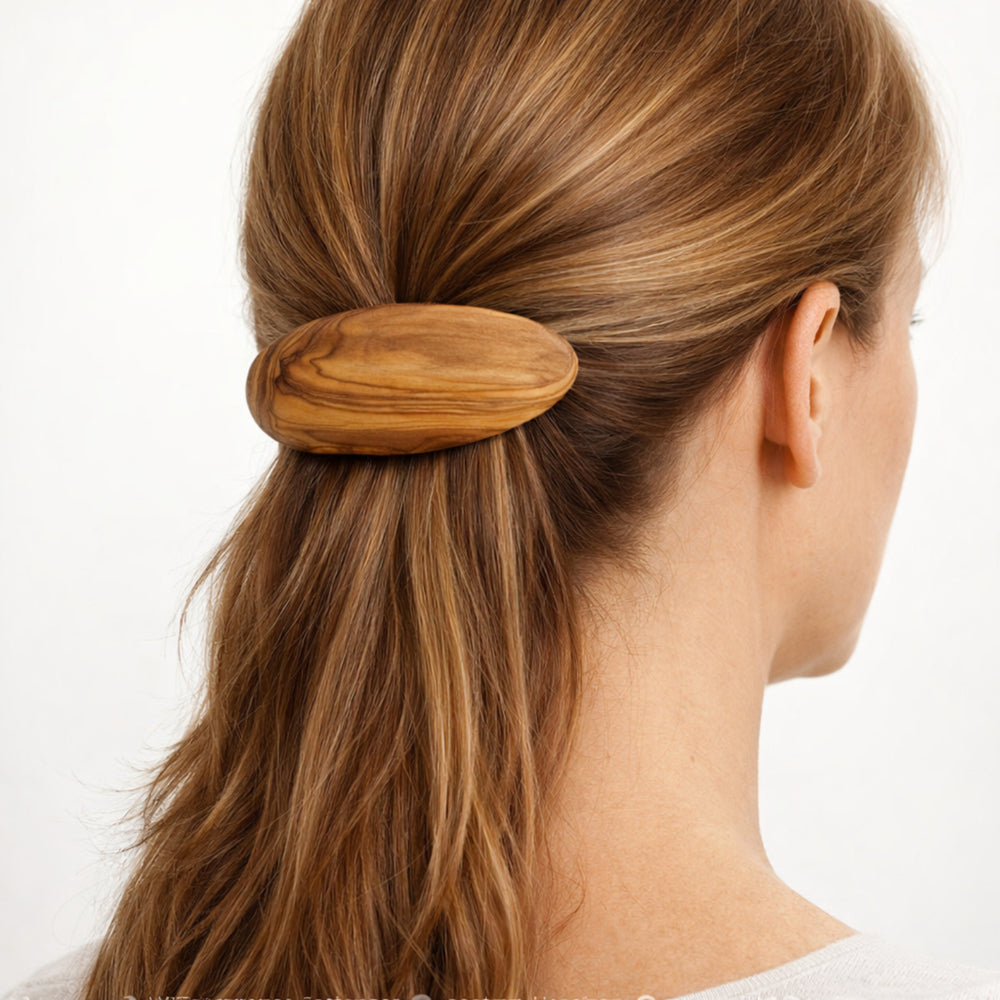 Olivenholz-Haarspange im Haar einer Frau, Rückansicht des Kopfes mit zusammengebundenem Haar, neutraler heller Hintergrund.