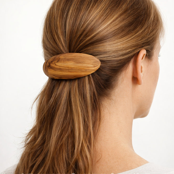 Olivenholz-Haarspange im Haar einer Frau, Rückansicht des Kopfes mit zusammengebundenem Haar, neutraler heller Hintergrund.