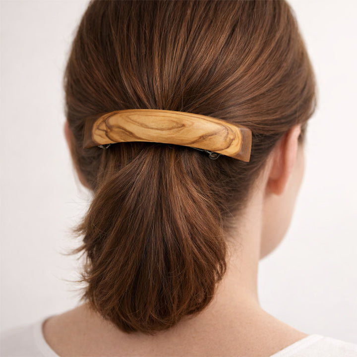 Olivenholz-Haarspange im Haar einer Frau, Rückansicht des Kopfes mit zusammengebundenem Haar, neutraler heller Hintergrund.