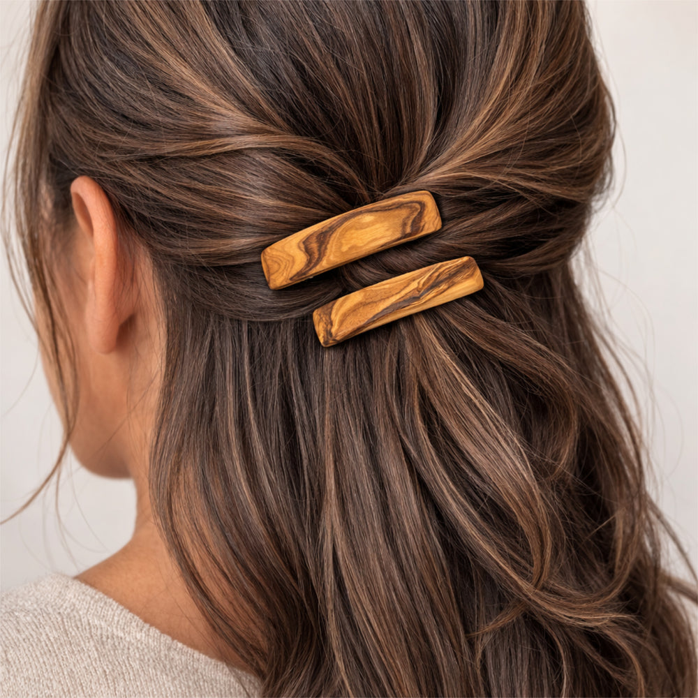 Olivenholz-Haarspange im Haar einer Frau, Rückansicht des Kopfes mit zusammengebundenem Haar, neutraler heller Hintergrund.