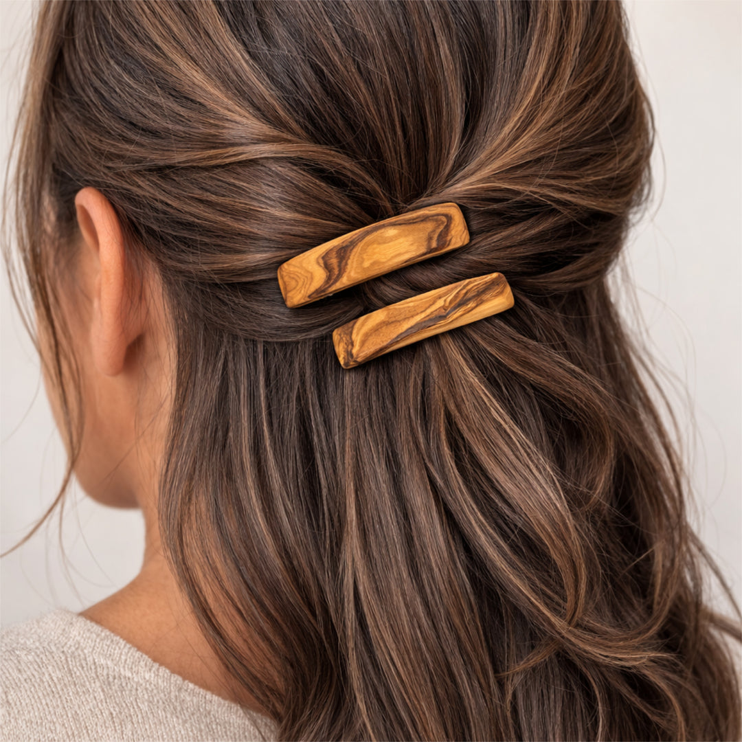 Olivenholz-Haarspange im Haar einer Frau, Rückansicht des Kopfes mit zusammengebundenem Haar, neutraler heller Hintergrund.