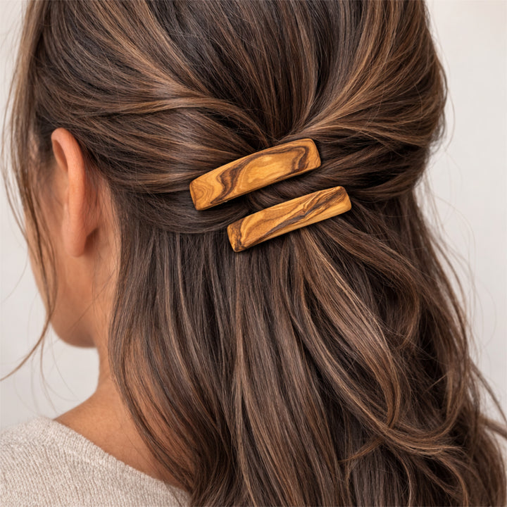 Olivenholz-Haarspange im Haar einer Frau, Rückansicht des Kopfes mit zusammengebundenem Haar, neutraler heller Hintergrund.